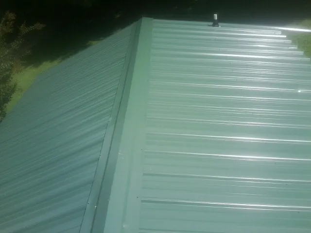 New green metal panels meeting at the ridge of a roof — Flat Roof Repair work by our crew in Waynesboro