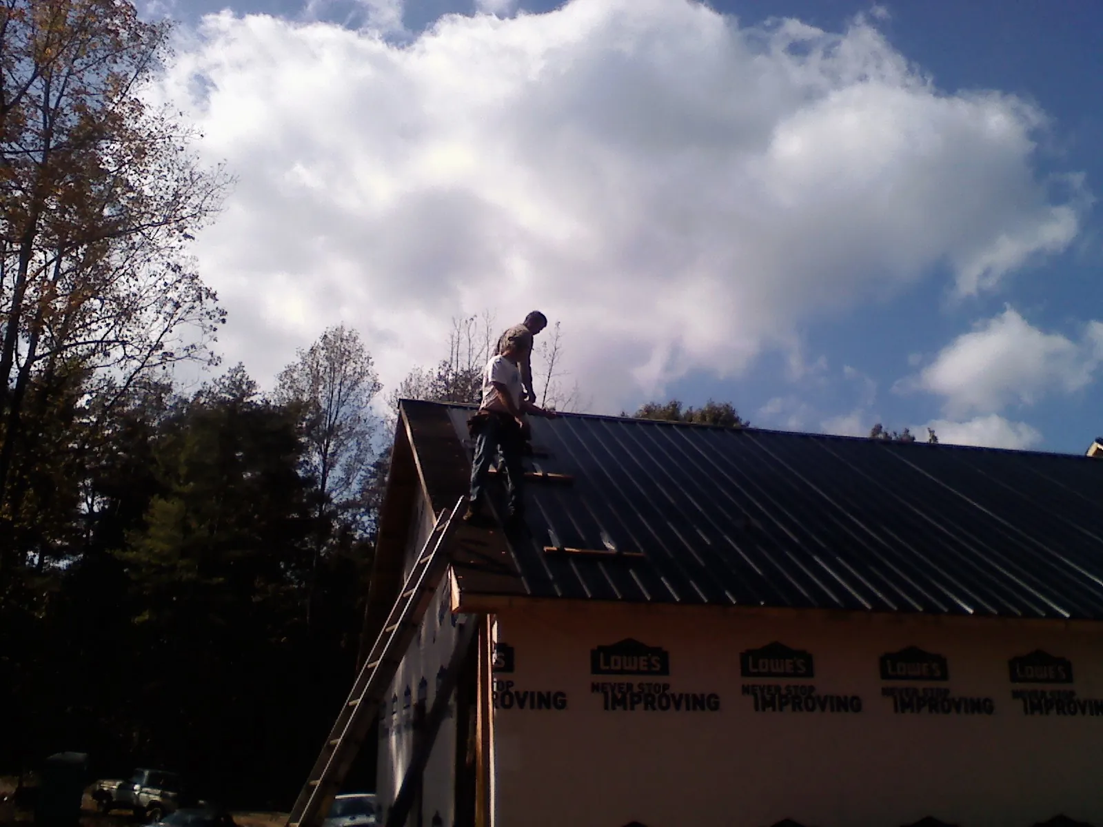 Roofer fastening dark metal panels high against a cloudy sky, from a Roof Inspection job in Waynesboro